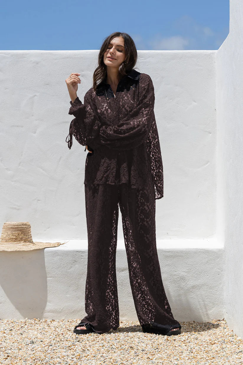 Woman in a dark lace outfit standing against a white wall with blue sky.