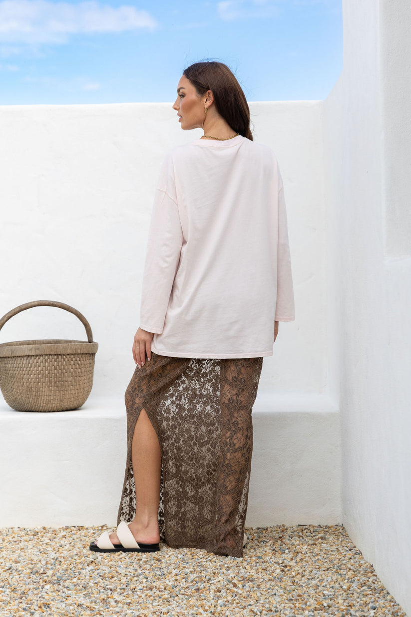 Woman in a white top and brown patterned skirt standing against a white wall with a blue sky.