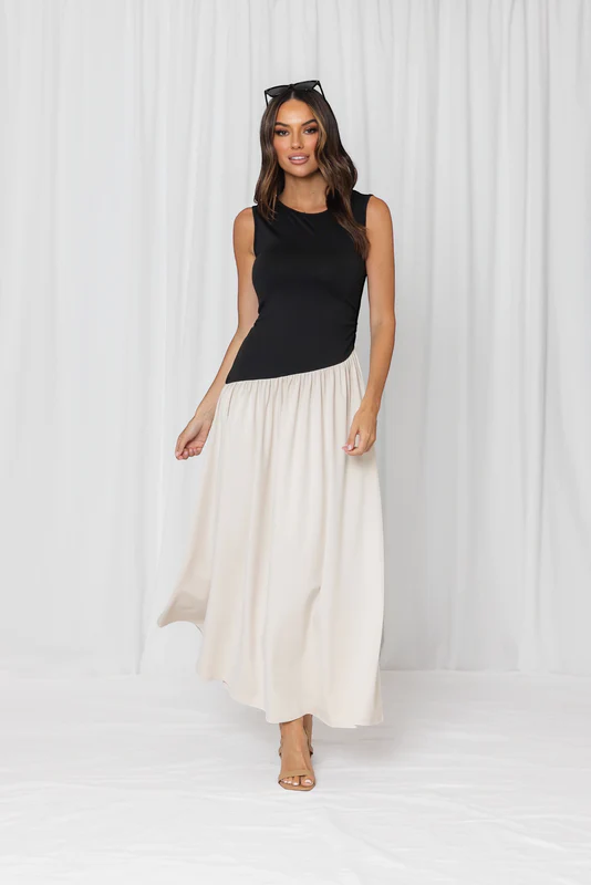 Woman wearing a black sleeveless top and white flowing skirt against a white background