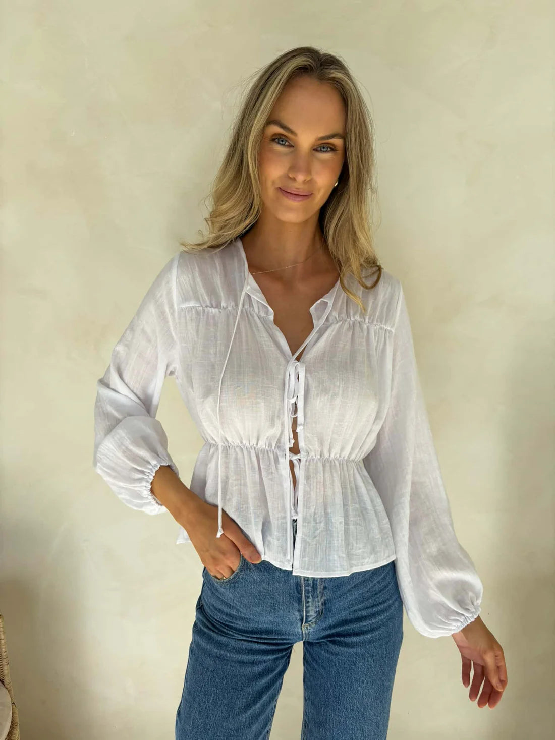 Woman wearing a white blouse and blue jeans against a plain background