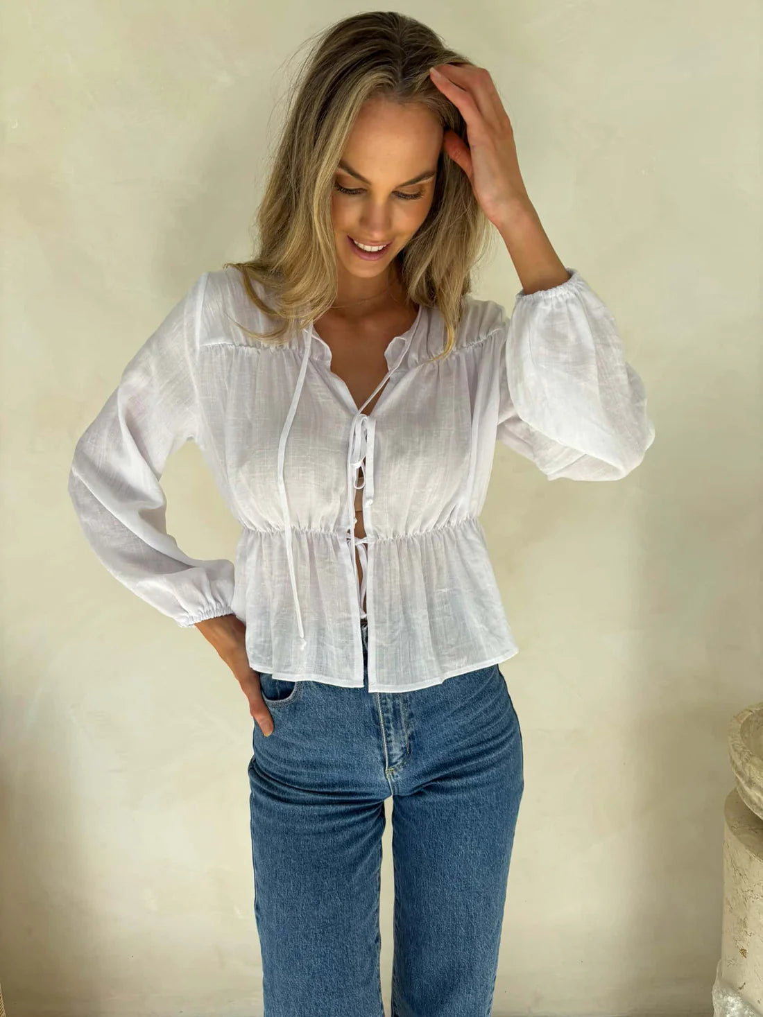 Woman wearing a white blouse and blue jeans against a beige background