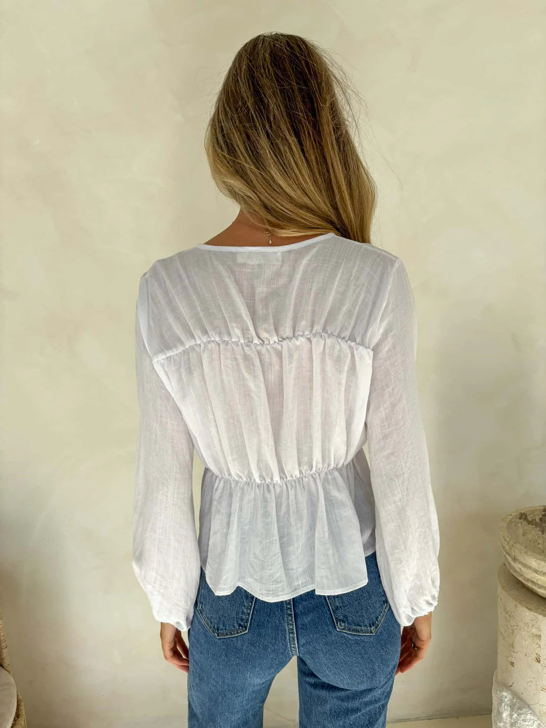 Person wearing a white blouse and blue jeans against a plain background