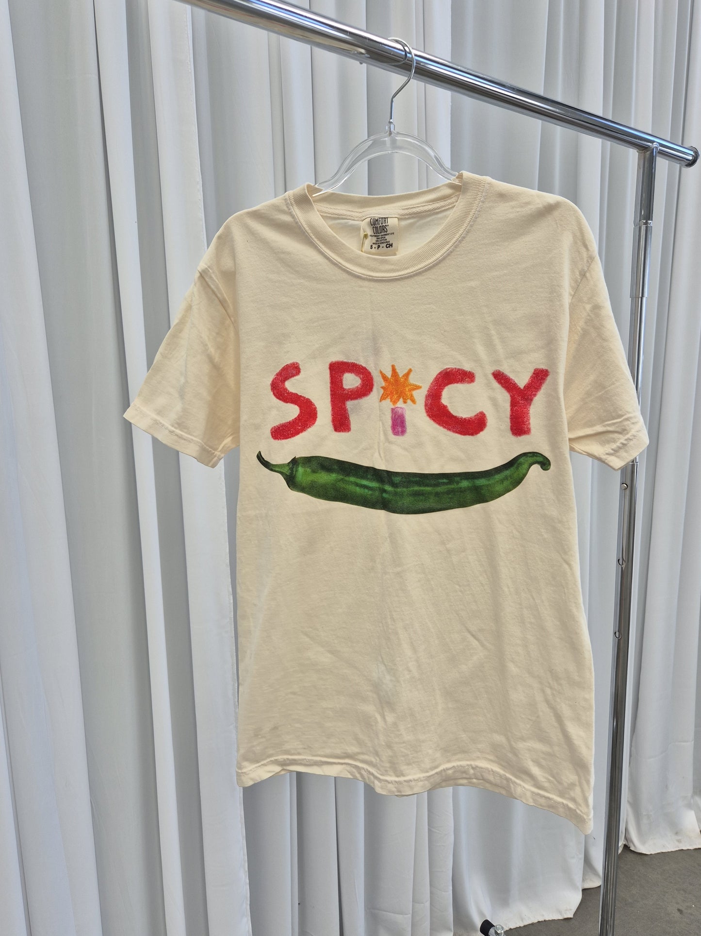 Front view of a soft cotton t-shirt in a light cream color, featuring a spicy  graphic design on the chest. The t-shirt has a crew neckline and short sleeves, perfect for casual wear or layering