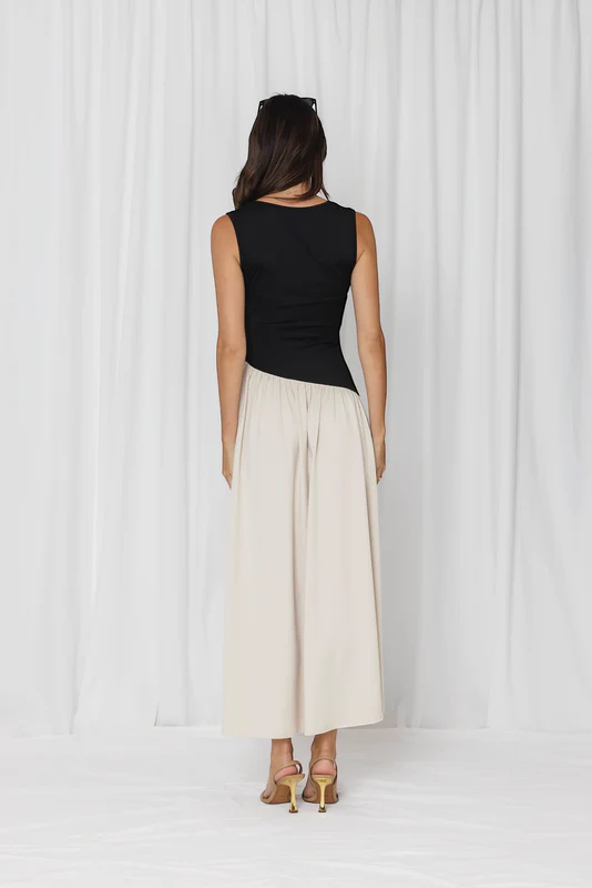 Person wearing a black sleeveless top and beige wide-leg pants on a white background